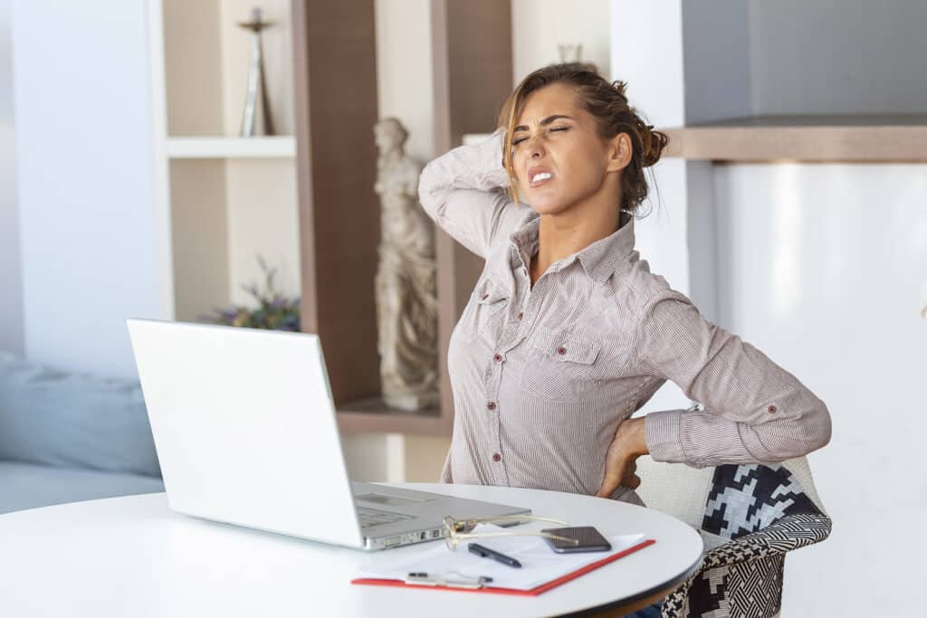 Woman experiencing back pain while working at a home office desk
